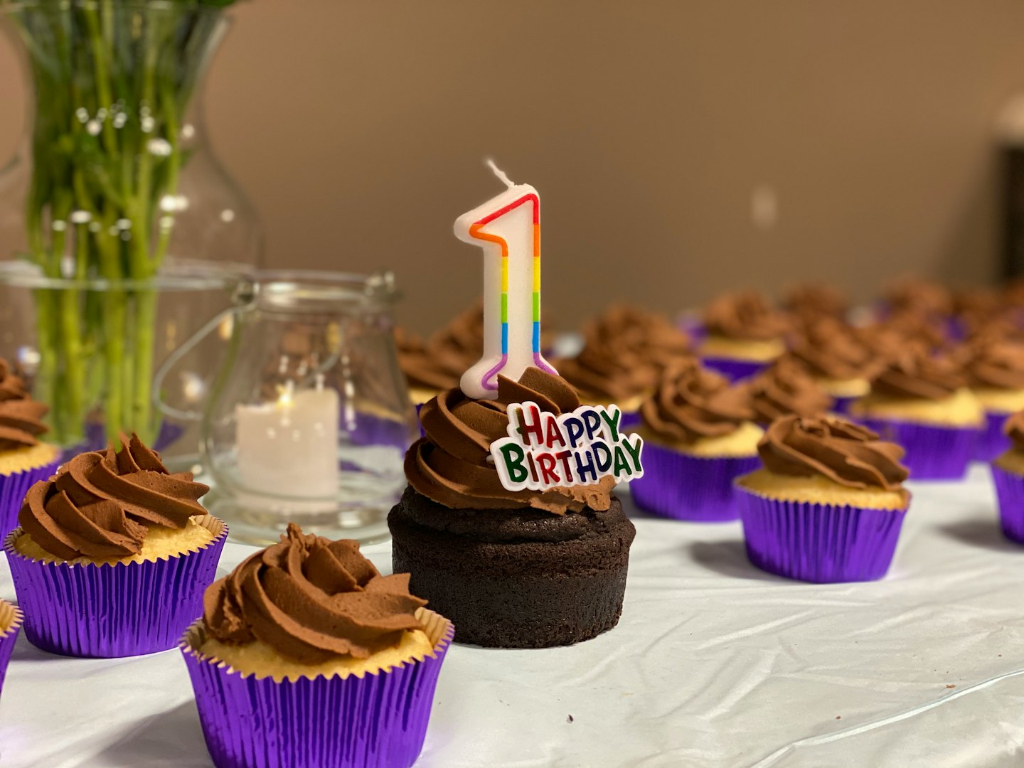 Chocolate cupcakes with candles sit on a birthday celebration table.