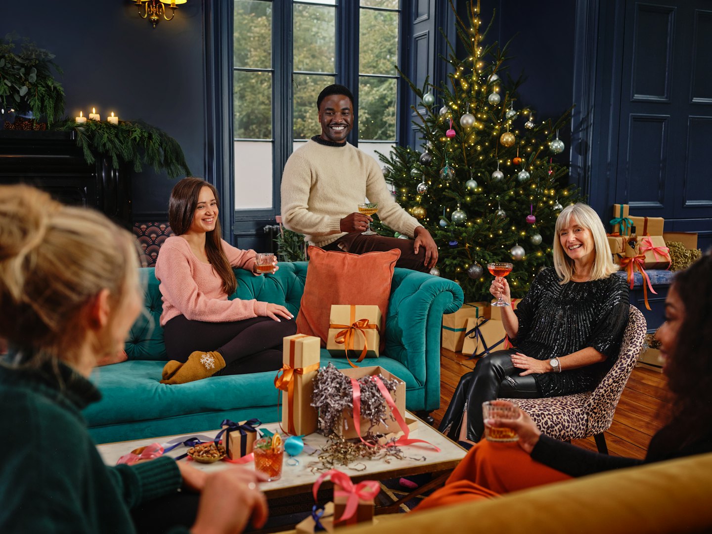 Diverse friends celebrate with drinks and gifts around a coffee table.