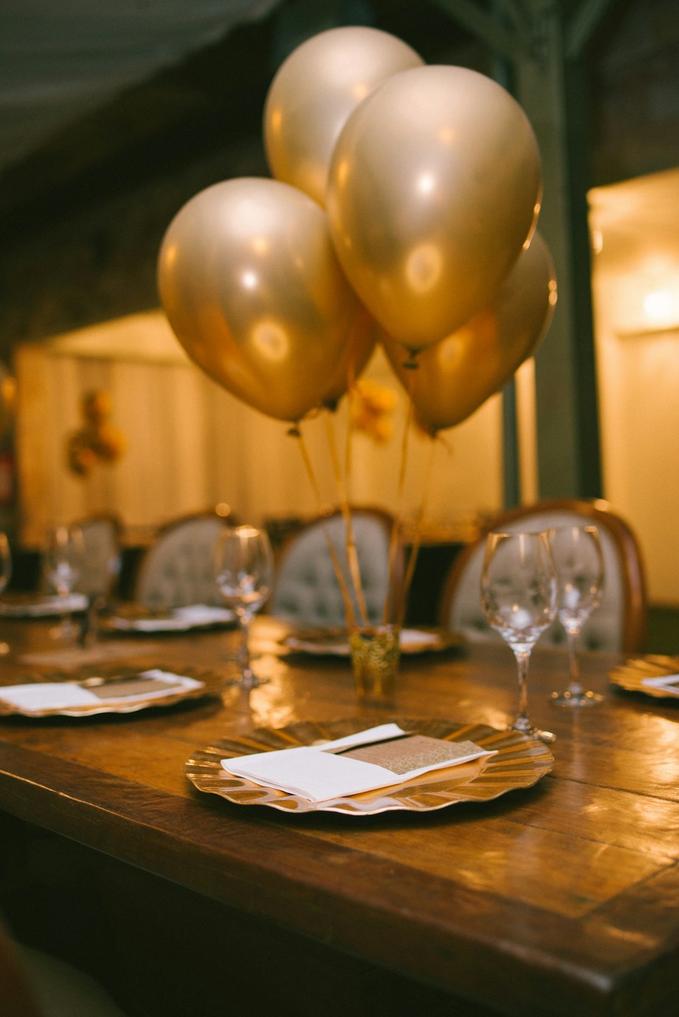 Dining table set with gold plates and balloons for a celebration.