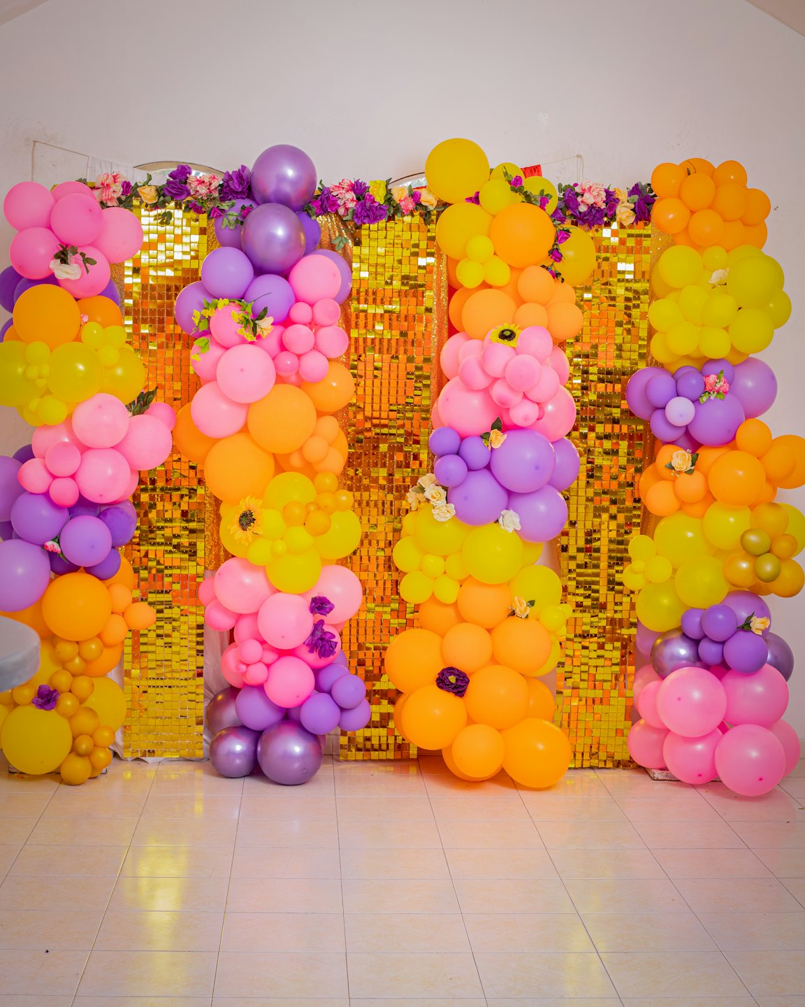 Colorful balloon columns stand in front of a gold sequin wall.