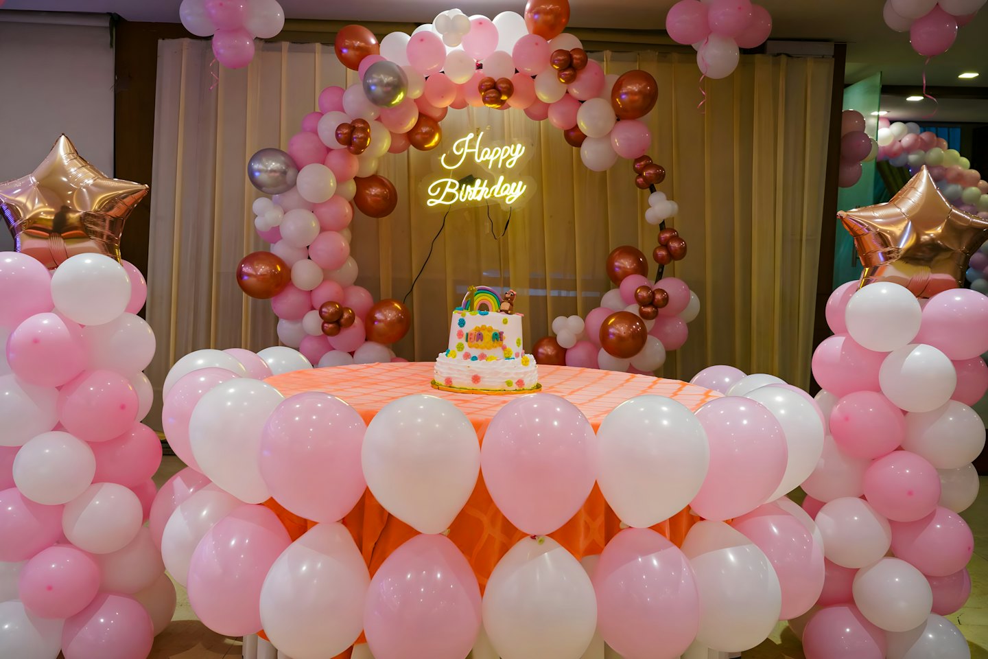Multi-tiered birthday cake sitting under a glowing neon sign.