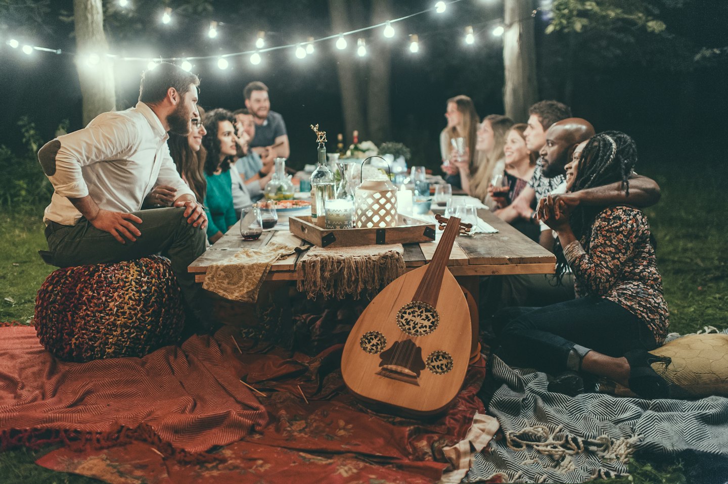 Friends enjoy an outdoor dinner party under string lights.