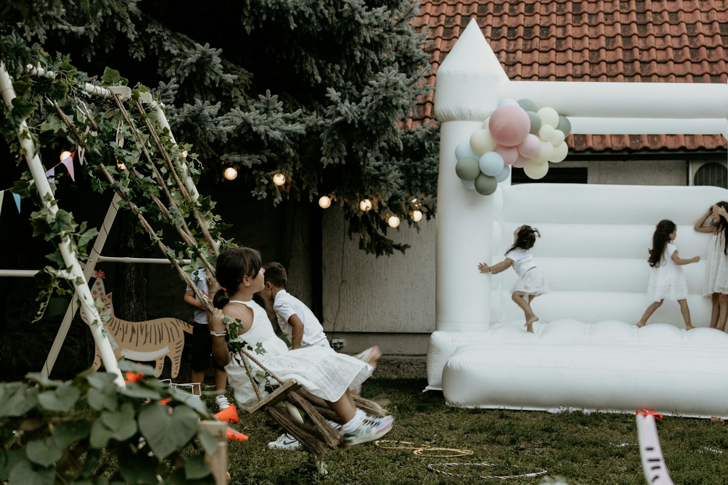 Children play on a swing set and inflatable castle outdoors.