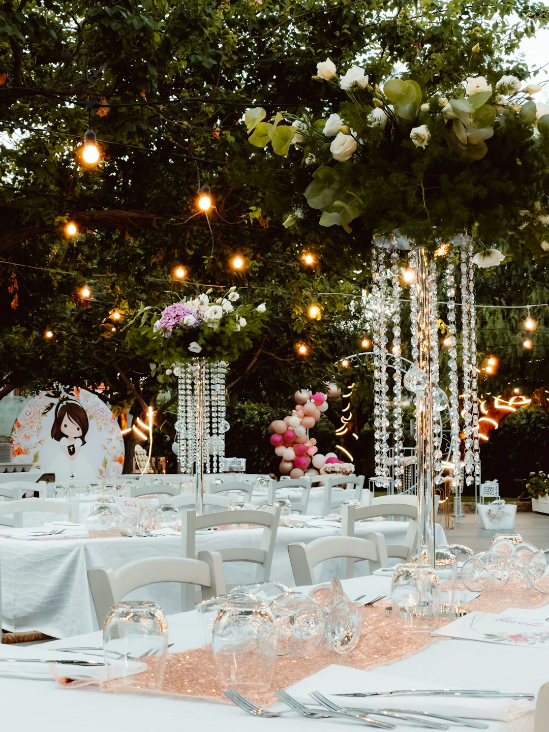 Outdoor event tables with floral centerpieces and string lights.